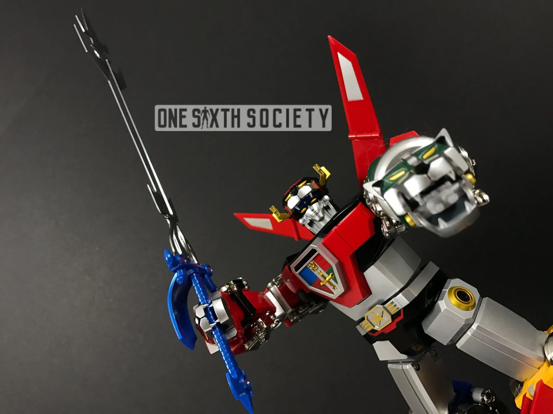 Low-angle view of Voltron GX-71 raising its sword, with the green lion-head arm extended toward the camera and red fins behind its shoulders.