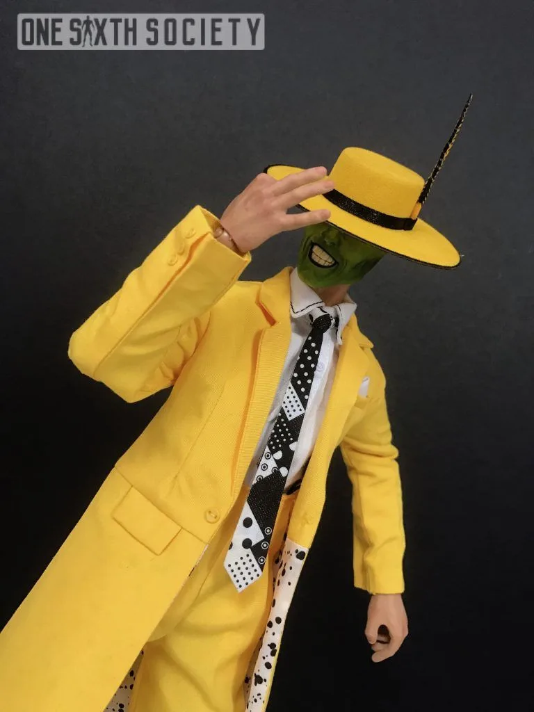 Closer view of The Mask figure tilting his yellow hat over his green face, showing the long coat and patterned tie.