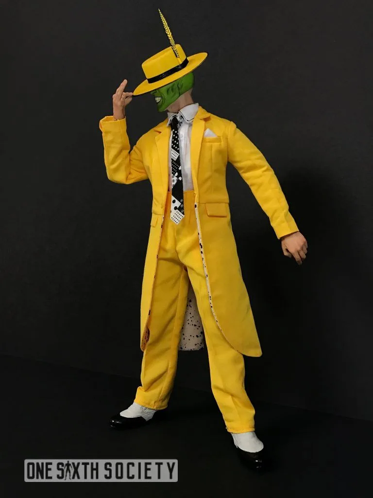 The Mask figure tipping a yellow feathered hat, wearing a matching long coat and trousers with a patterned black-and-white tie.
