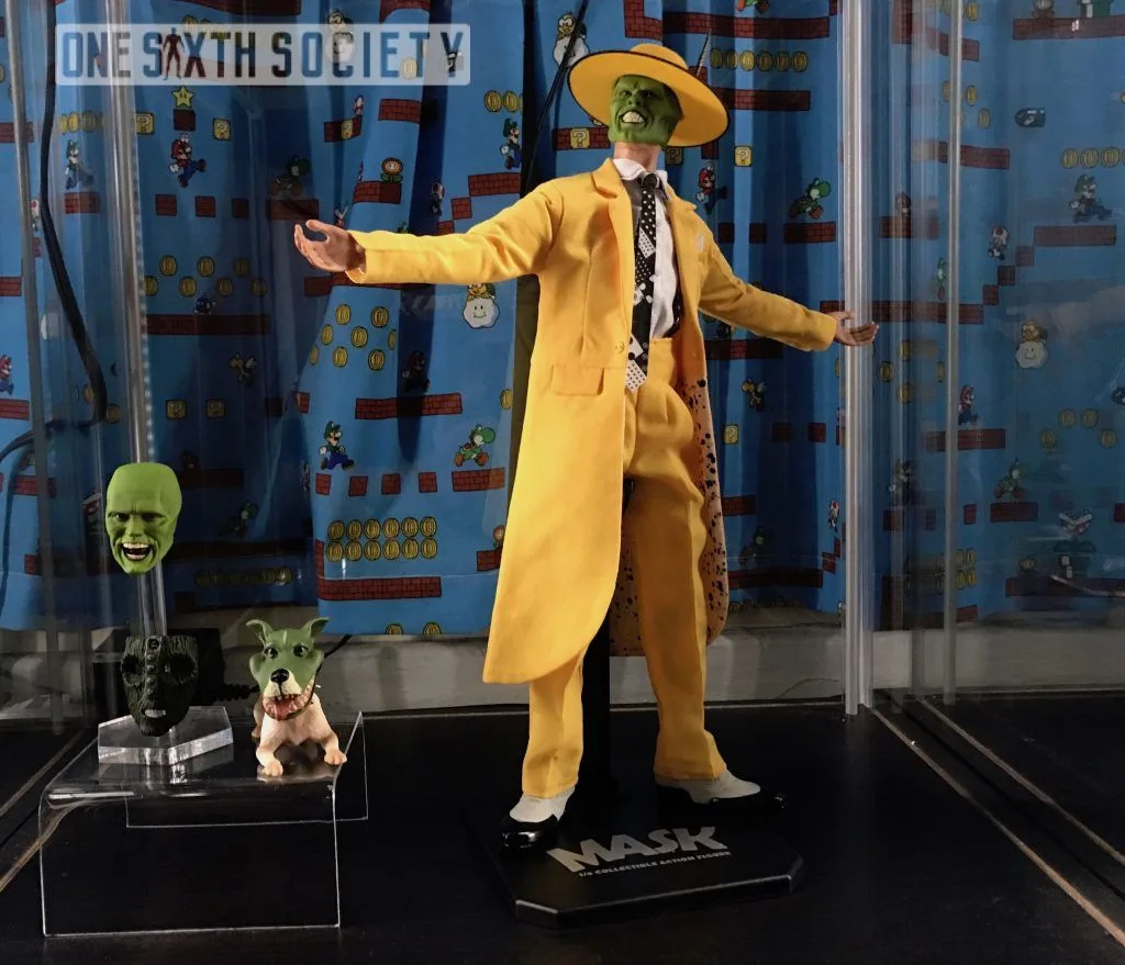 The Mask figure with arms spread on a labelled stand beside an alternate green head, the mask prop and a small dog figure.
