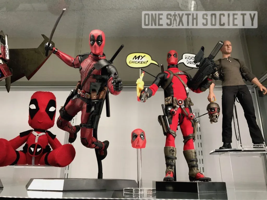 Glass cabinet with a posed Hot Toys Deadpool and a standing custom Deadpool, comic speech bubbles, a rubber chicken and other collectibles.