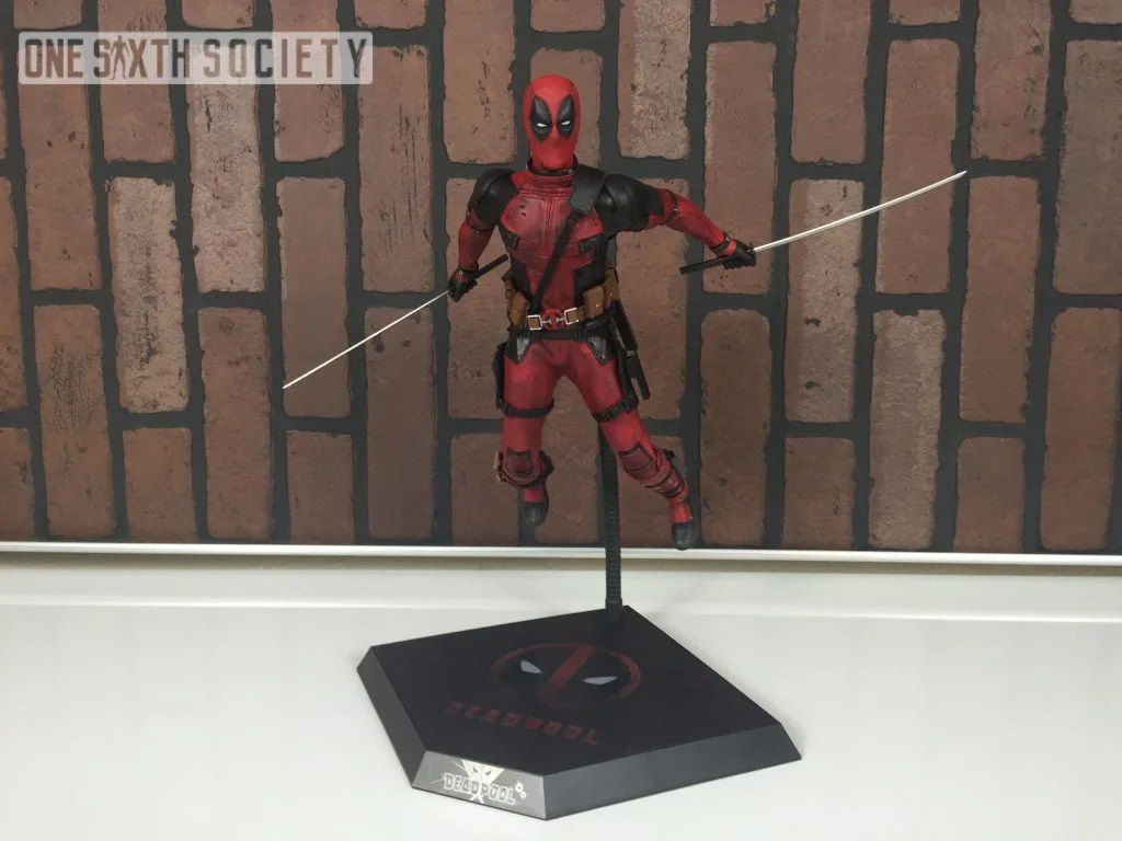 Deadpool figure leaning forward on a black dynamic stand with one leg bent and two swords extended outward.