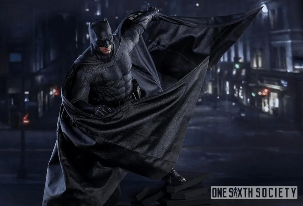 Hot Toys Batman figure raising one side of his black cape while the other folds across his body against a nighttime city backdrop.