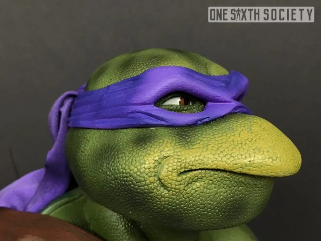 Close-up of NECA Donatello's face showing the purple mask, painted brown eye, green skin texture and closed mouth.