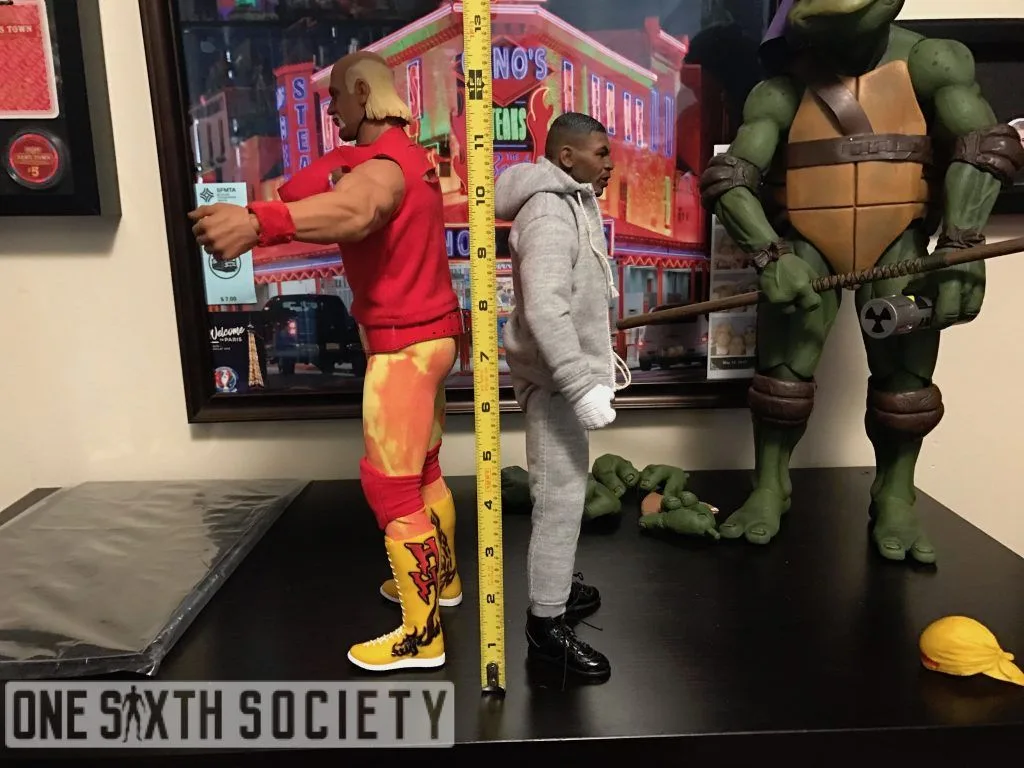 Hulk Hogan and Mike Tyson figures standing back to back beside a measuring tape, with a larger Ninja Turtle figure behind them.