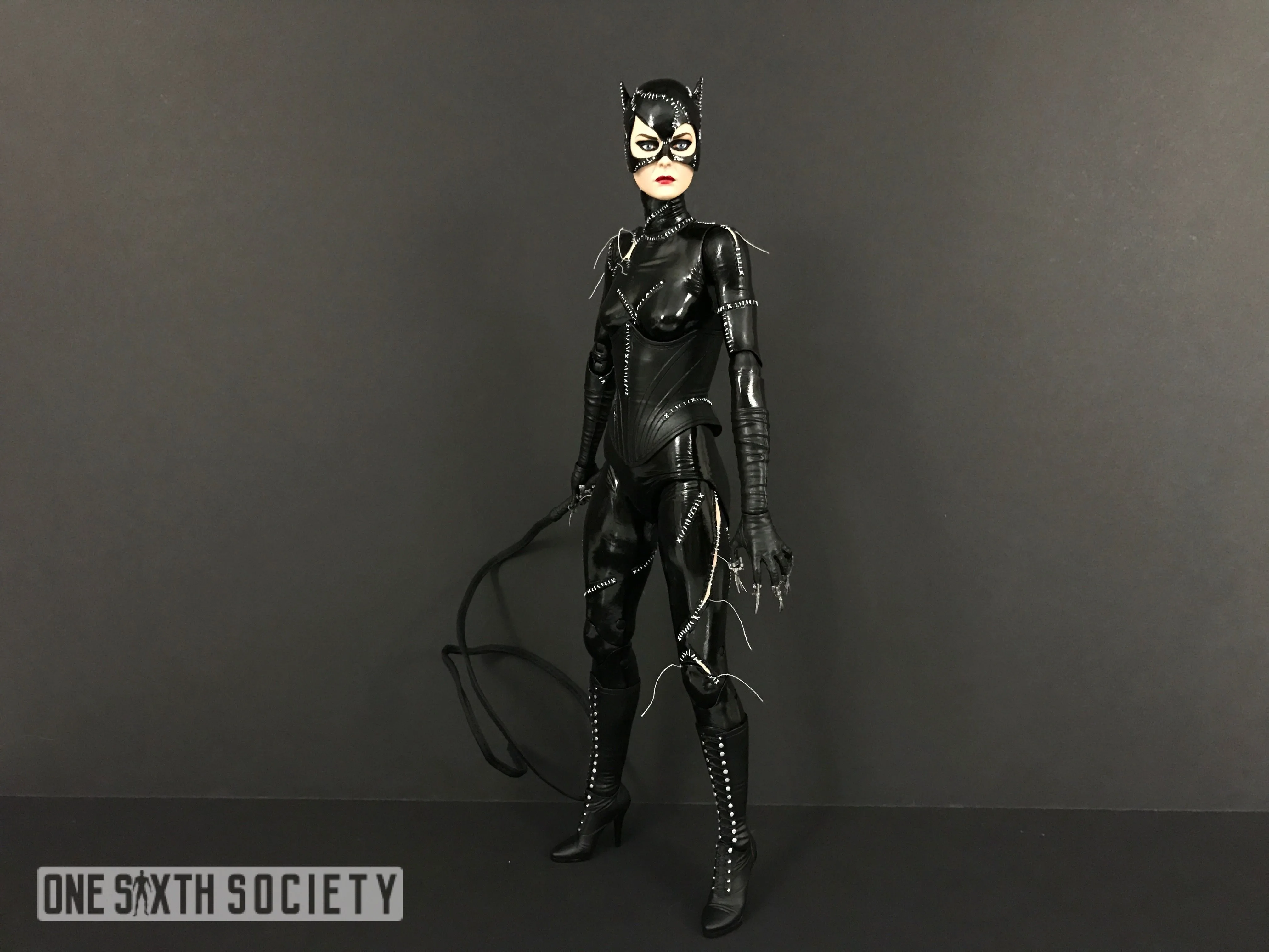 Full-length NECA Catwoman in a glossy black stitched catsuit and tall boots, holding a looped whip at her side.