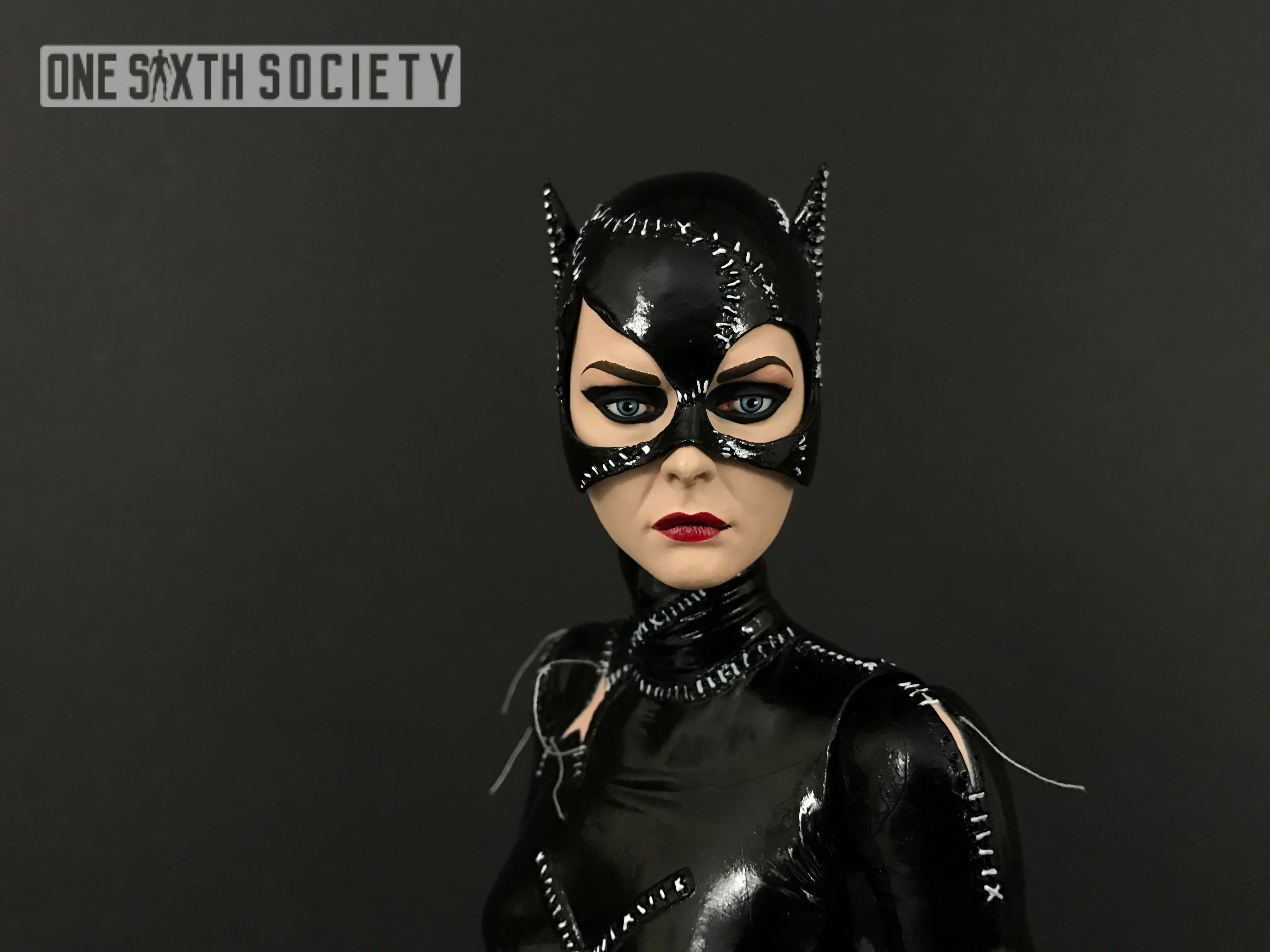 Close-up of NECA Catwoman's intact black mask with pointed ears, white stitching, blue eyes and dark red lips.