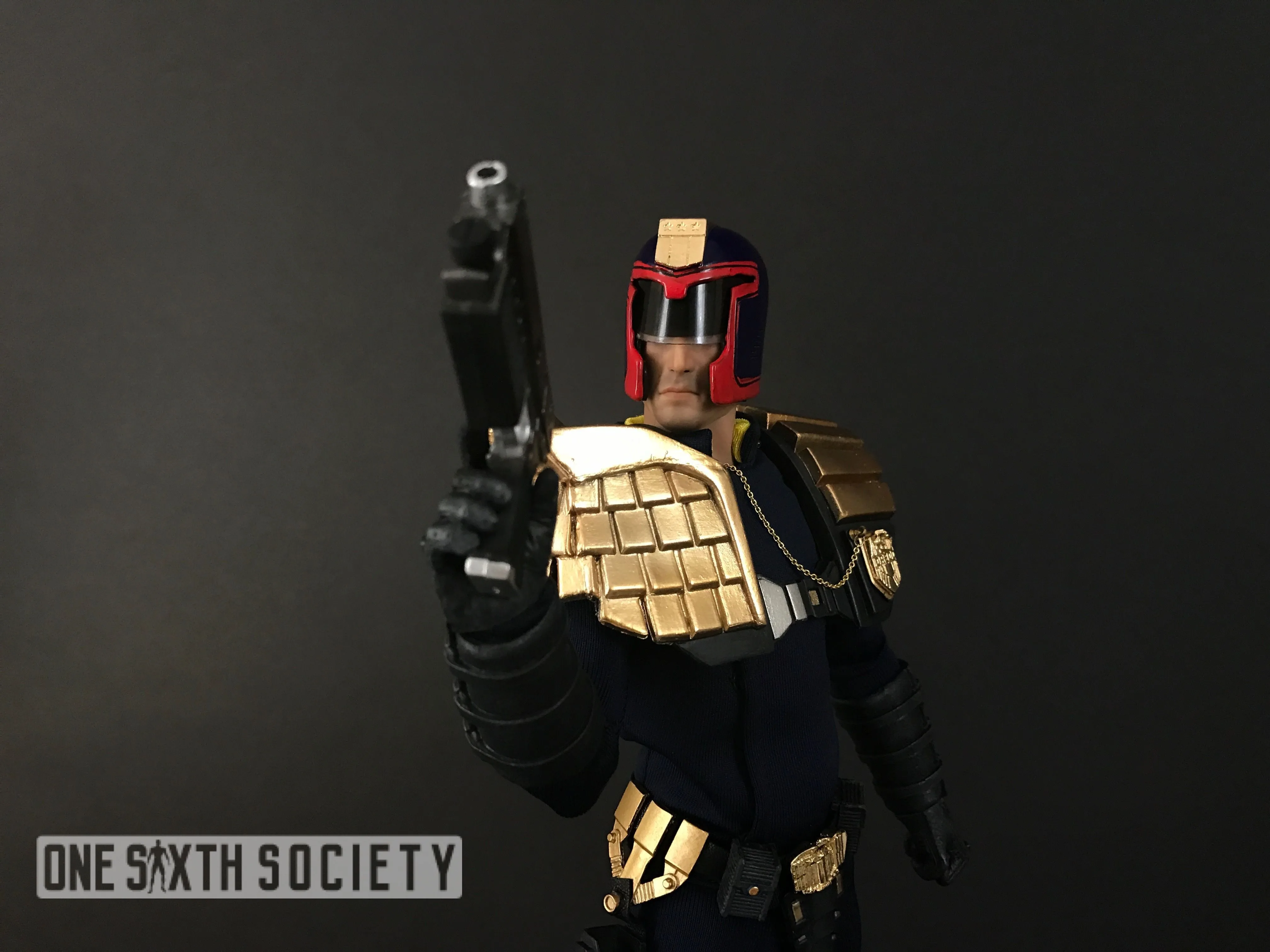 Judge Dredd figure aiming a black pistol toward the camera, with gold shoulder armor and a red-trimmed helmet.