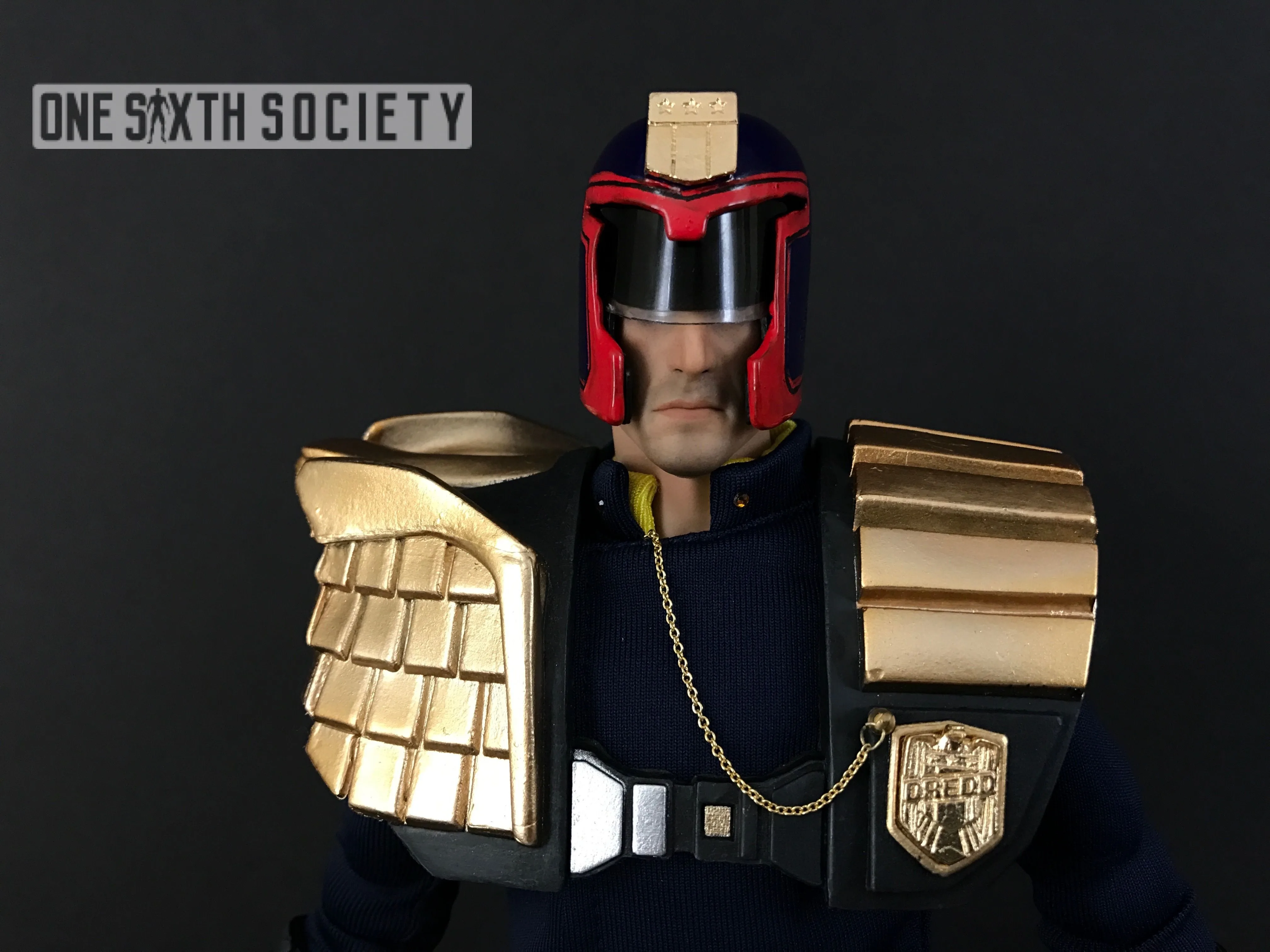 Front view of Judge Dredd's gold shoulder pads, chained chest badge and red-trimmed helmet with a black visor.