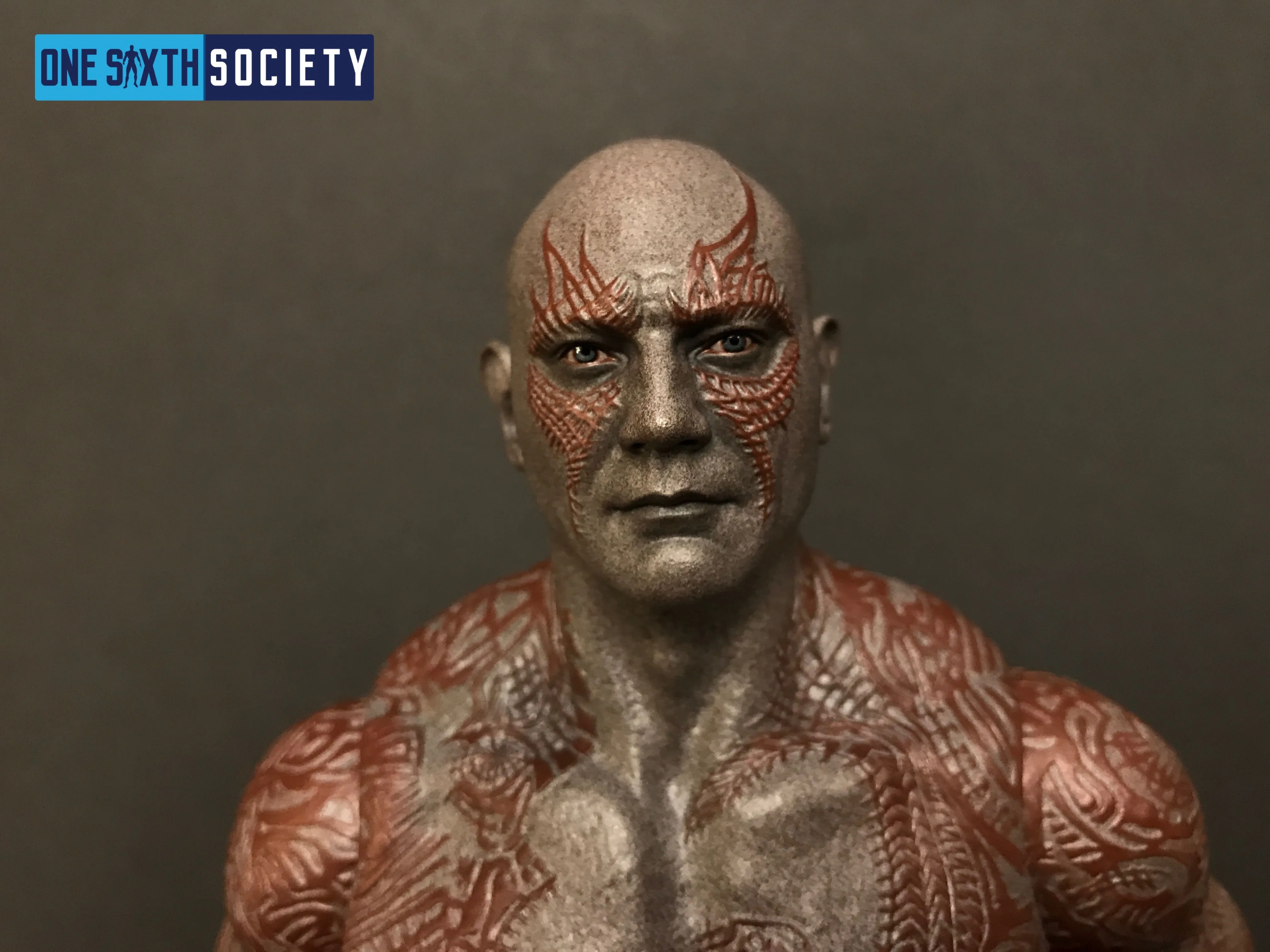 Close-up of the Hot Toys Drax head and shoulders, showing a stern expression and raised red tattoo patterns across gray skin.