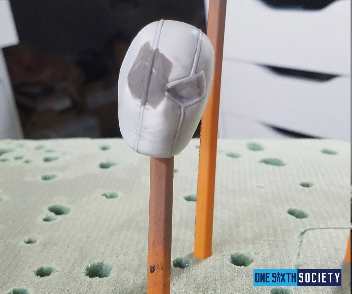 Unpainted white mask mounted on a stick, with a gray modified area around one eye for the custom Deathstroke head.