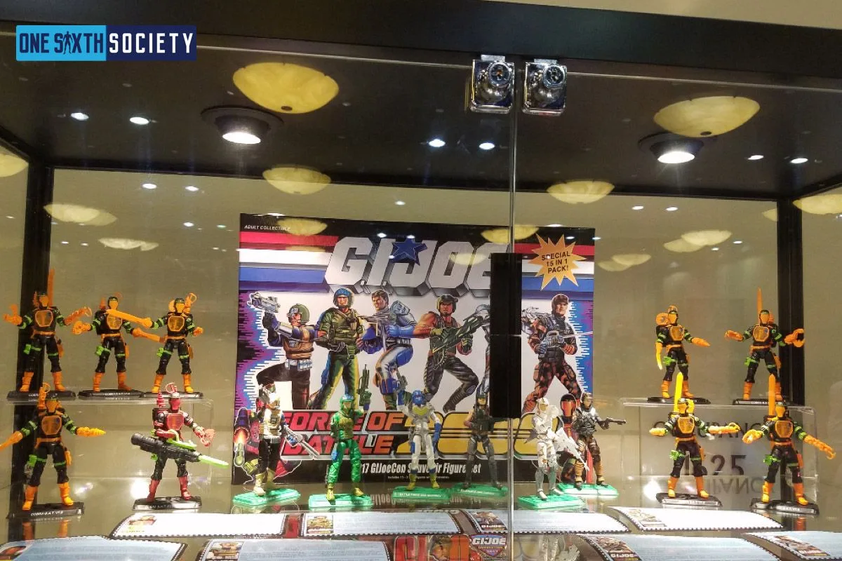 G.I. Joe figures arranged in a glass case around the Force of Battle 2000 convention set artwork at JoeCon 2017.