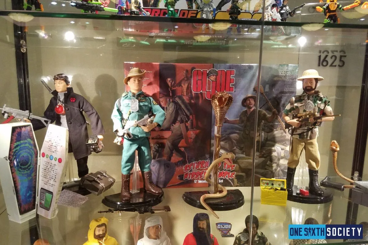 Three G.I. Joe explorer figures share a glass shelf with equipment, packaging and a raised cobra model.