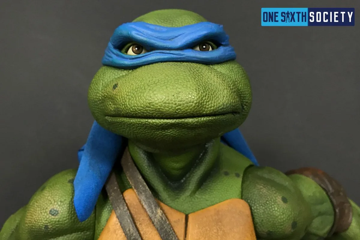 Front close-up of NECA Leonardo's head sculpt, showing the blue mask, textured green skin and calm closed-mouth expression.