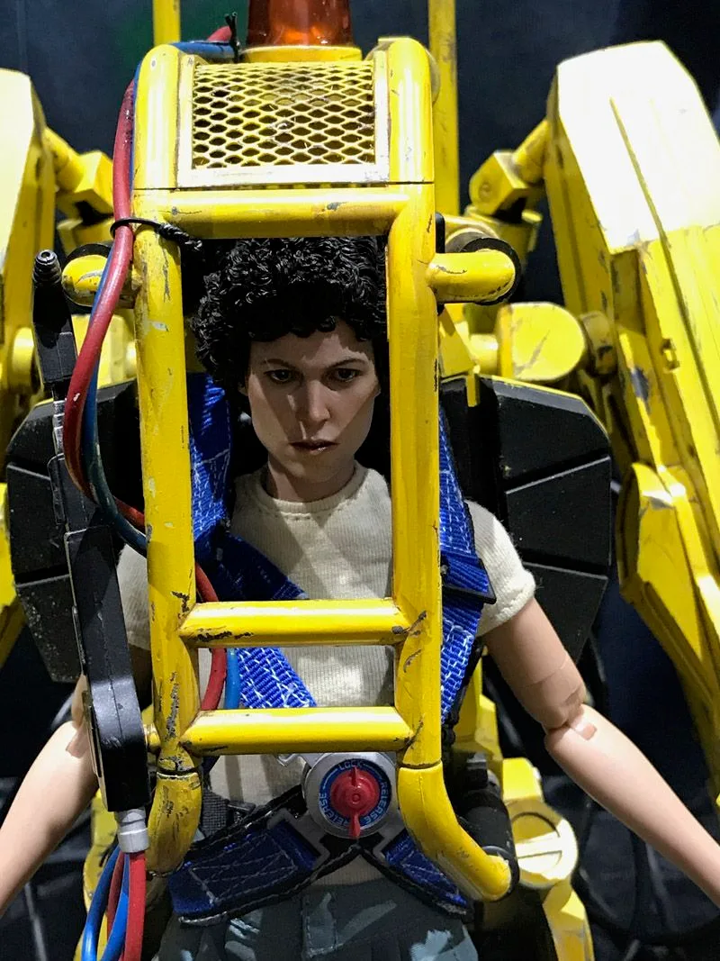 Hot Toys Ellen Ripley secured in a blue harness inside the yellow Power Loader, with its protective bars framing her head and torso.