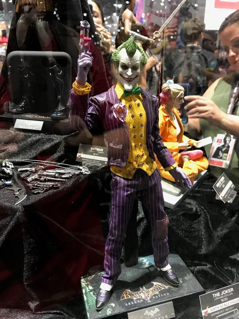 Hot Toys Joker with green hair, a purple striped suit, yellow waistcoat and green bow tie, holding a pistol upright.