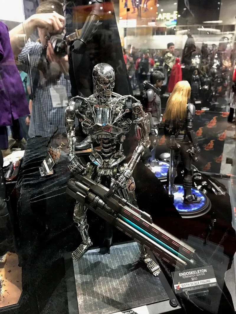 Hot Toys Terminator endoskeleton with exposed metallic joints, holding a large weapon across its body on a grated display base.
