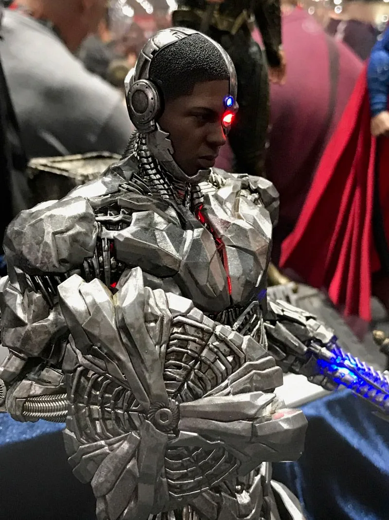 Close-up of Hot Toys Cyborg’s silver chest and arm mechanisms, with red and blue face lights and a blue-lit weapon extending from one arm.