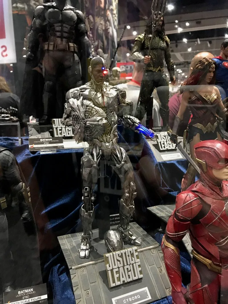Hot Toys Cyborg in silver mechanical armor on a Justice League base, with a blue-lit arm weapon and other team figures behind him.