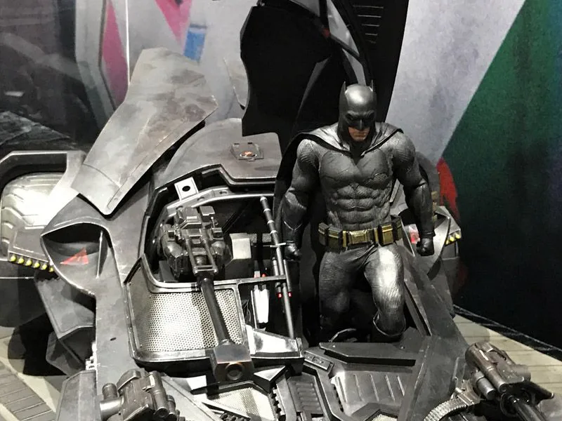 Close view of Hot Toys Batman kneeling beside the Batmobile’s open cockpit, with the seat, central gun and dashboard details visible.