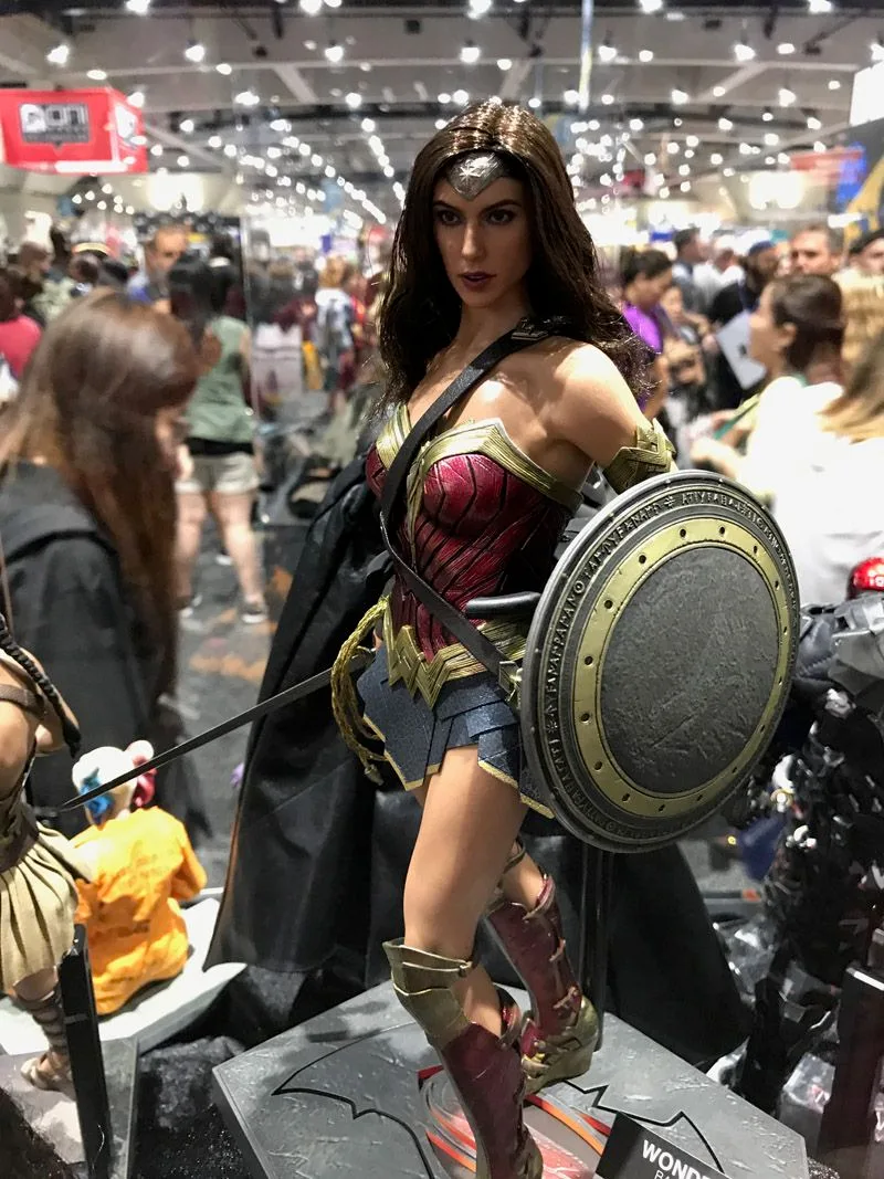 Hot Toys Wonder Woman in red, blue and gold armor, holding a sword and large round gray shield in the convention display.