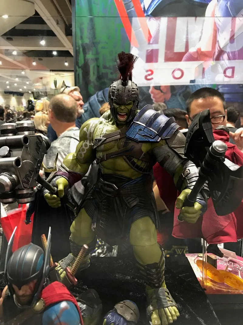 Hot Toys Gladiator Hulk roaring beneath a crested helmet, wearing blue shoulder armor and gripping two large weapons.