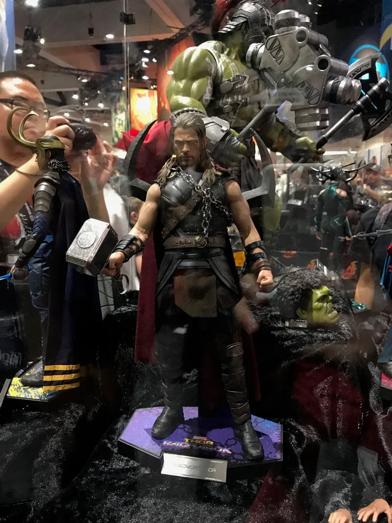 Hot Toys Thor shown full length holding Mjolnir, with long hair, a dark armored outfit and a red cape.