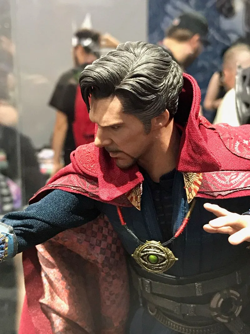 Hot Toys Doctor Strange with gray-streaked hair, a red patterned cloak and the Eye of Agamotto, turning toward his extended arm.