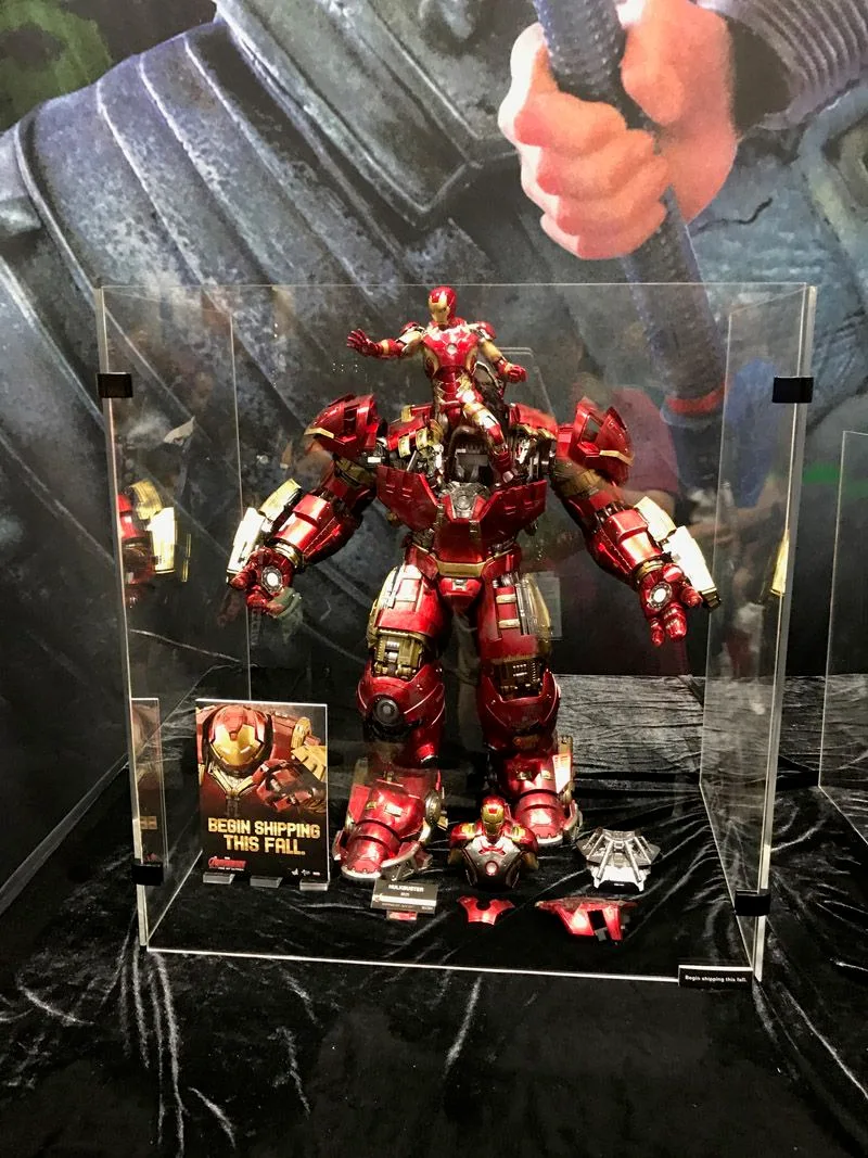 Hot Toys Hulkbuster displayed inside a clear case with its upper armor open and an Iron Man figure rising above the bulky red-and-gold suit.