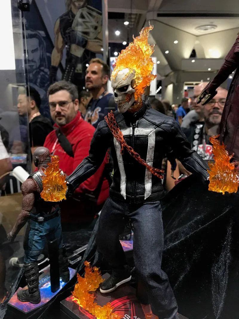 Hot Toys Ghost Rider with a flaming skull, black jacket and white chest design, surrounded by flame effects and a fiery chain.