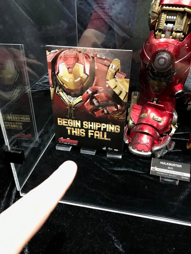 A visitor points toward the Hulkbuster display sign reading “Begin Shipping This Fall” at Comic-Con 2017; the figure’s red armored foot is beside it.