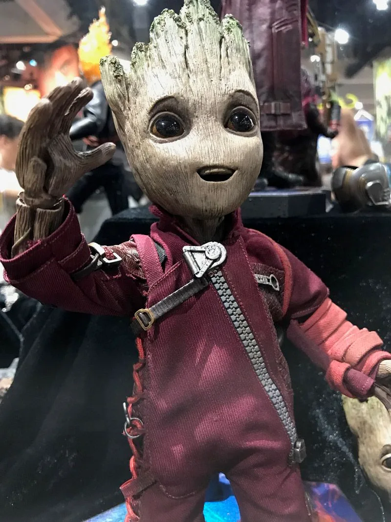 Hot Toys Groot in a red Ravager jumpsuit, smiling with one wooden hand raised beside his head.