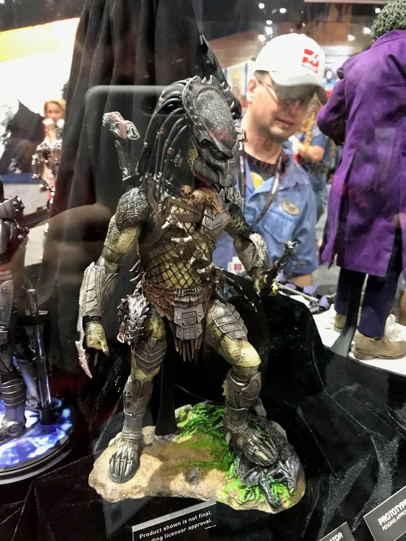 Hot Toys Predator standing in a wide stance on a rocky base with green details, wearing a mask, netted bodysuit and layered armor.