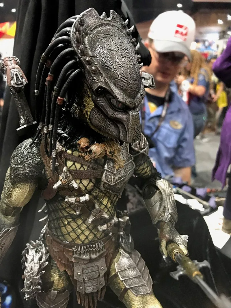Hot Toys Predator close-up showing a textured mask, long dark head tendrils, netted torso and small skull trophies across the chest.