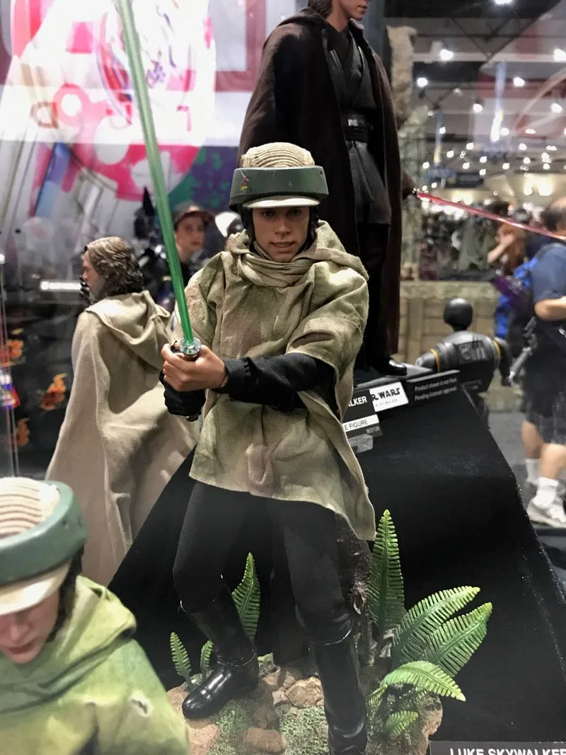 Closer view of Hot Toys Endor Luke Skywalker gripping a green lightsaber with both hands, wearing a helmet, tan-green poncho and black boots.