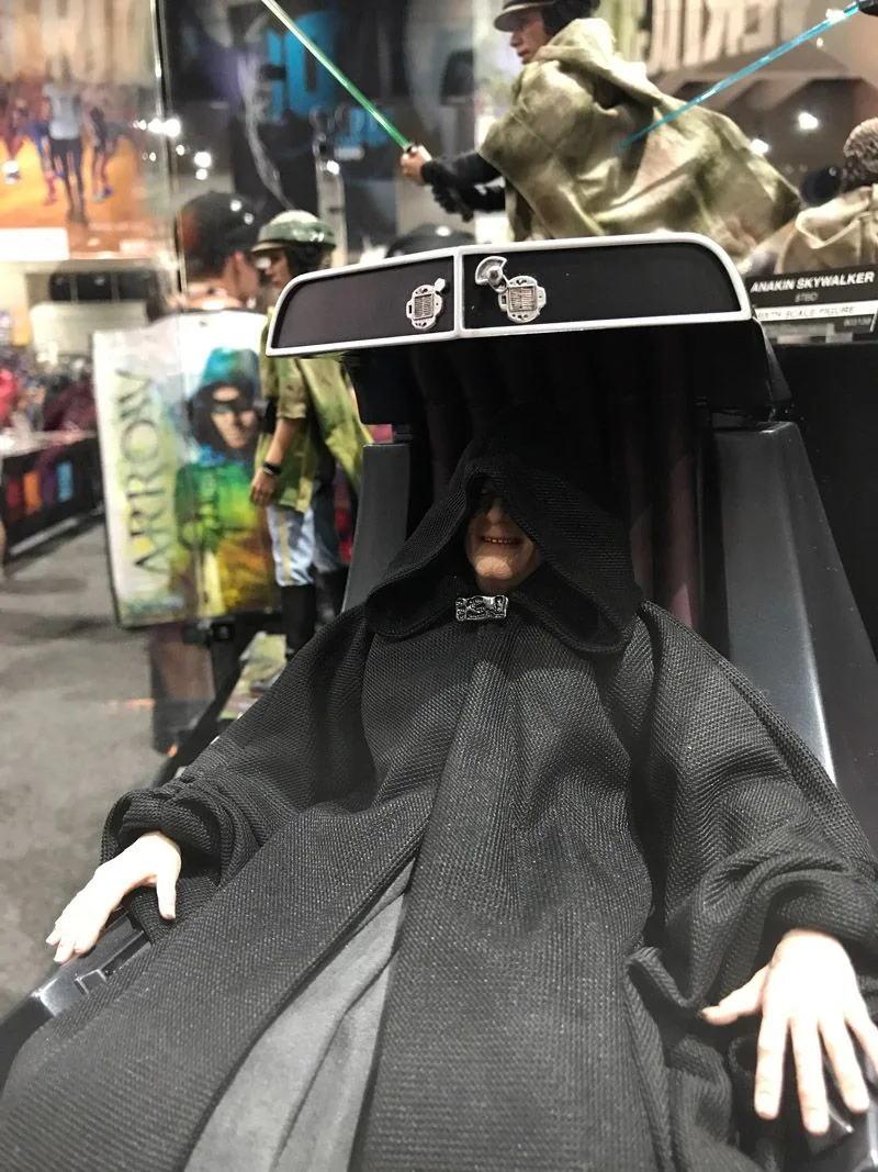Hot Toys Emperor Palpatine seated in a tall black throne, with his hood low over his face and pale hands resting near the armrests.