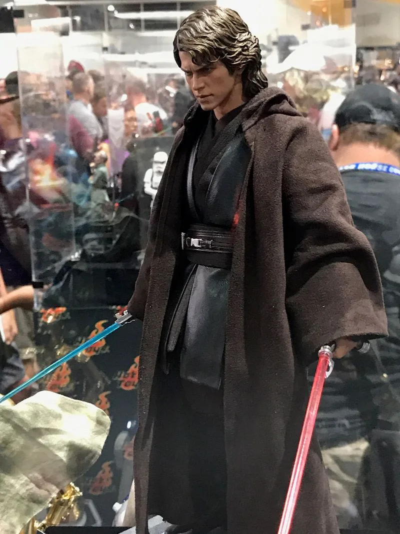 Hot Toys Anakin Skywalker with wavy hair and layered dark Jedi clothing beneath a brown robe, with lightsaber blades visible beside him.