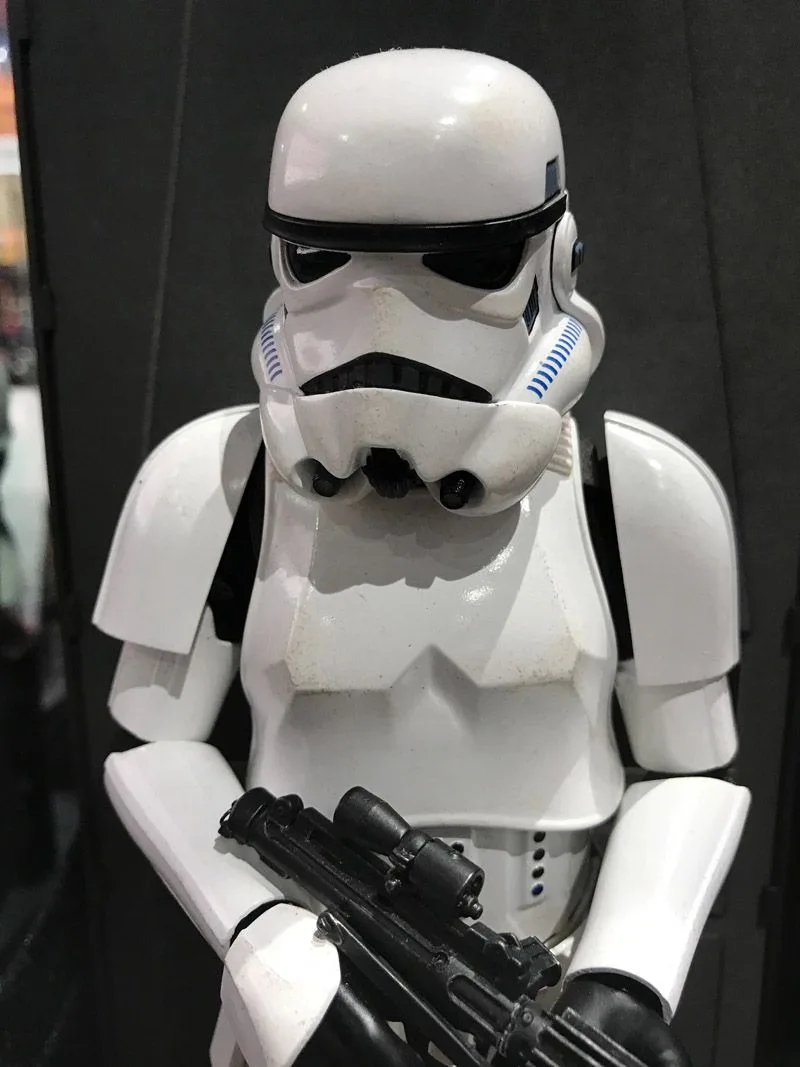 Close view of a Hot Toys Stormtrooper helmet and white chest armor, with a black blaster held in both hands.