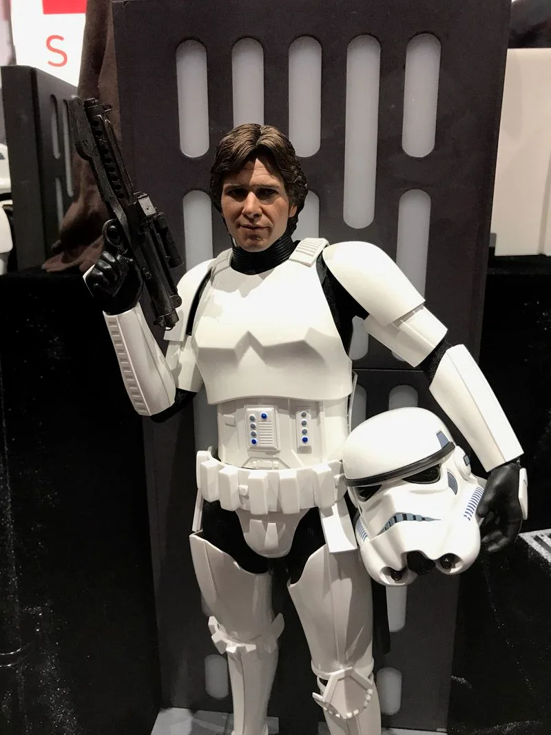 Closer view of Hot Toys Han Solo wearing Stormtrooper armor, with his face uncovered, blaster raised and helmet held at his hip.