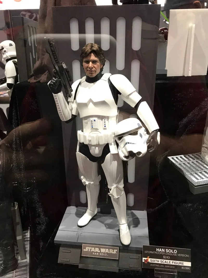 Hot Toys Han Solo in white Stormtrooper armor, holding a blaster and helmet in front of a gray wall-panel backdrop.