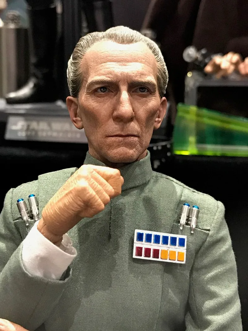 Close-up of Hot Toys Grand Moff Tarkin with gray hair, lined features and a raised hand, showing his colored Imperial rank badge.