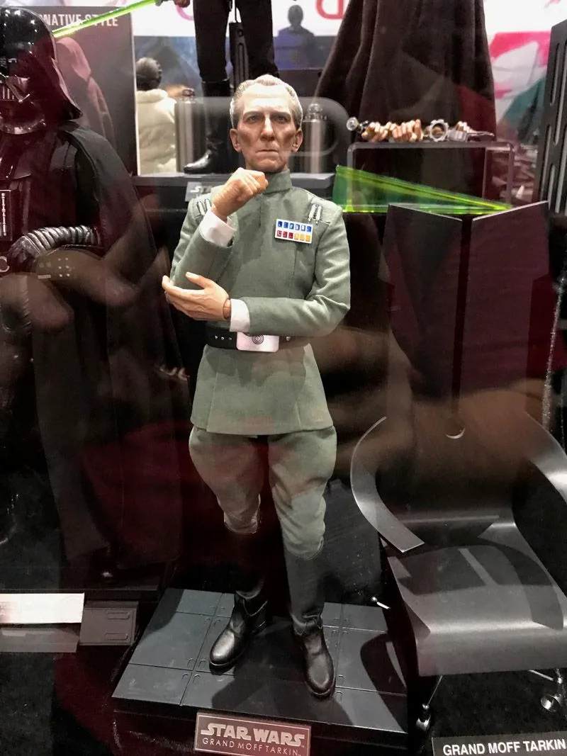 Hot Toys Grand Moff Tarkin in a gray-green Imperial uniform, posed with one hand at his chin on a Star Wars display base.