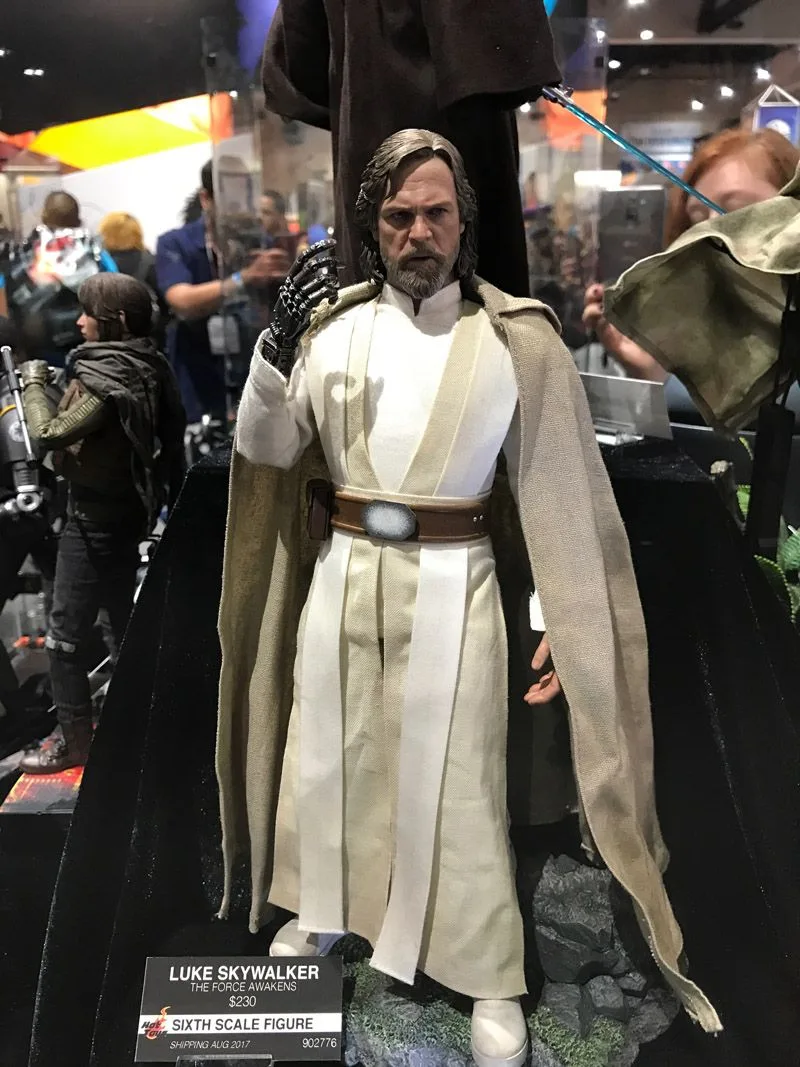 Hot Toys older Luke Skywalker with a gray beard, pale Jedi robes and tan cloak, raising his mechanical hand.