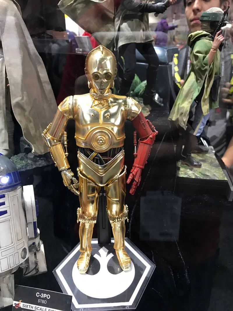 Hot Toys C-3PO in polished gold with a red left arm, standing on a black base with a white Resistance emblem.