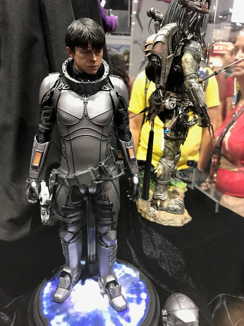Hot Toys Valerian in gray segmented armor on a blue-lit base, with his helmet displayed beside his feet and a Predator behind him.