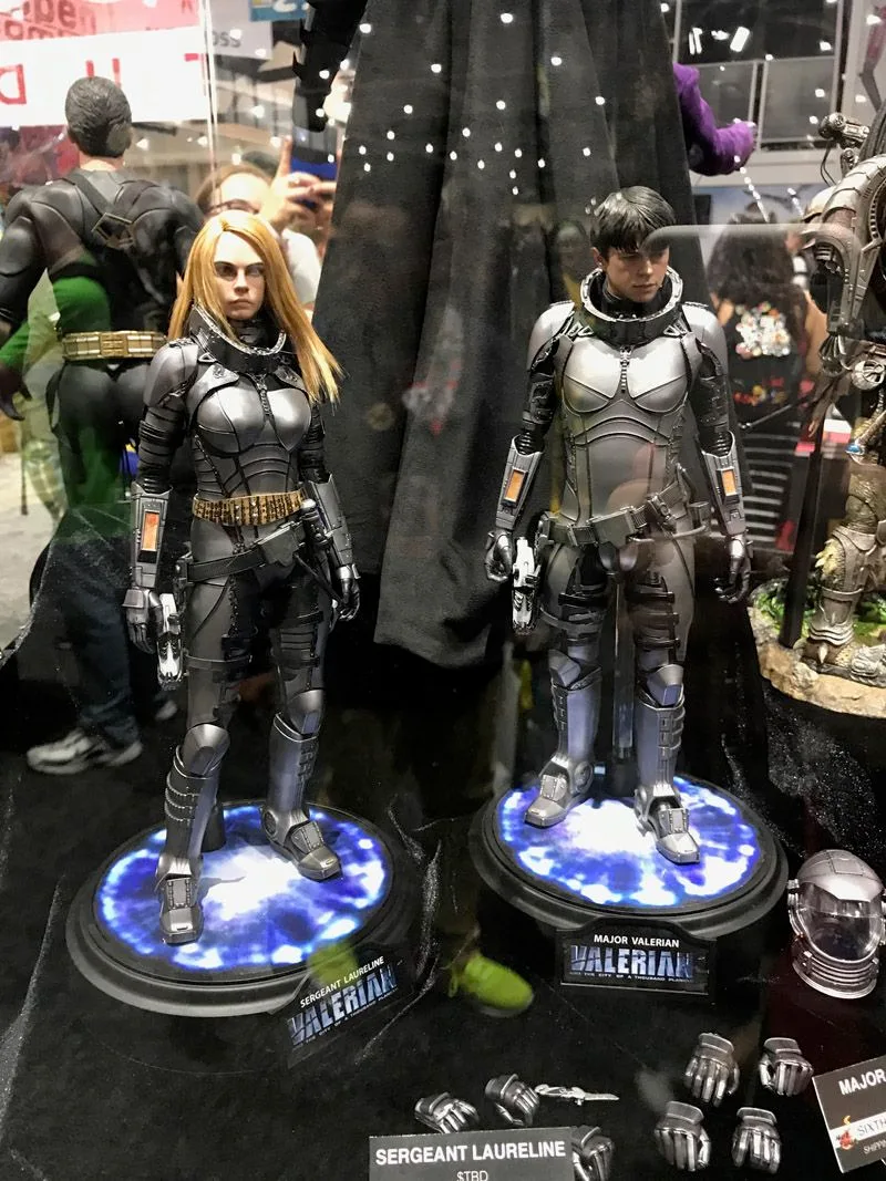 Hot Toys Laureline and Valerian in matching gray space armor on blue-lit circular bases, with spare hands and helmets displayed below.