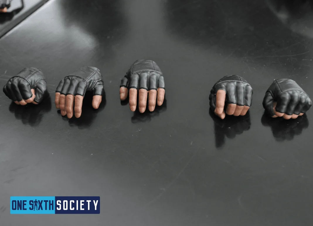 Five interchangeable Hot Toys Deadshot hands arranged on a dark tabletop, showing fingerless gloves and different grips.