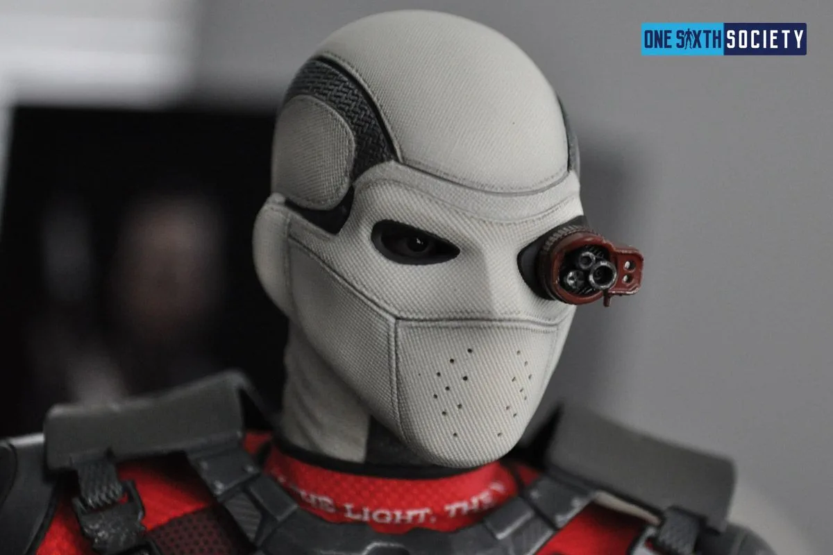 Hot Toys Deadshot wearing his textured white full-face mask with a dark eye opening and red side-mounted targeting scope.