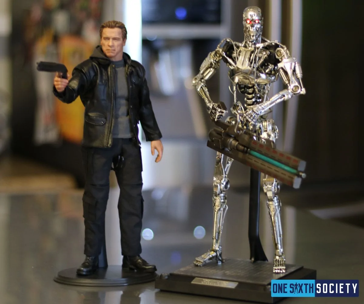 Hot Toys Guardian T-800 aiming a handgun beside the Genisys Endoskeleton holding its laser cannon, each on a separate display base.