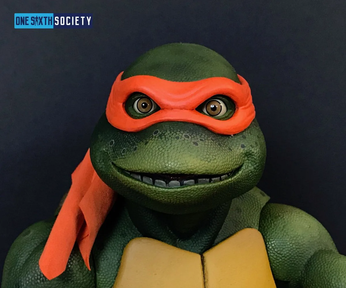 Close-up of NECA movie Michelangelo's smiling face, bright orange mask, brown eyes and textured green skin.